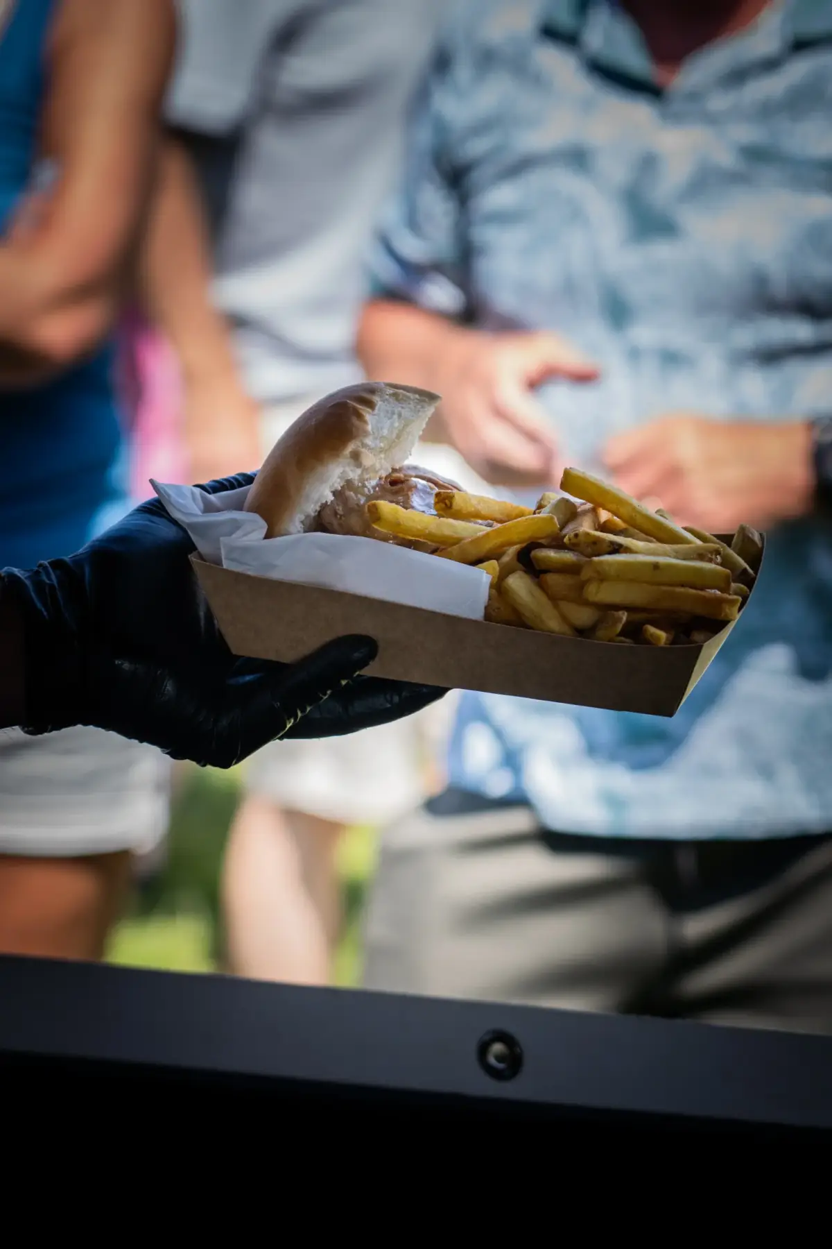 A burger and chips in a tray being handed to a customer at a street food stall
