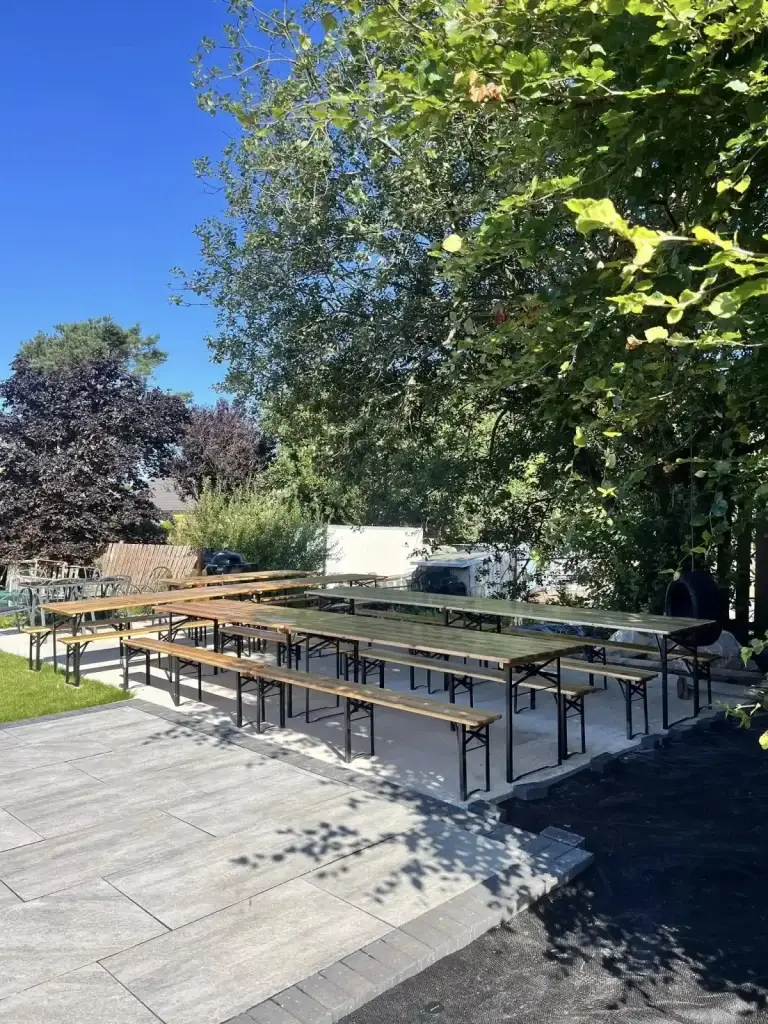 Outdoor seating setup with long tables and benches arranged for a christening event under sunny blue skies.