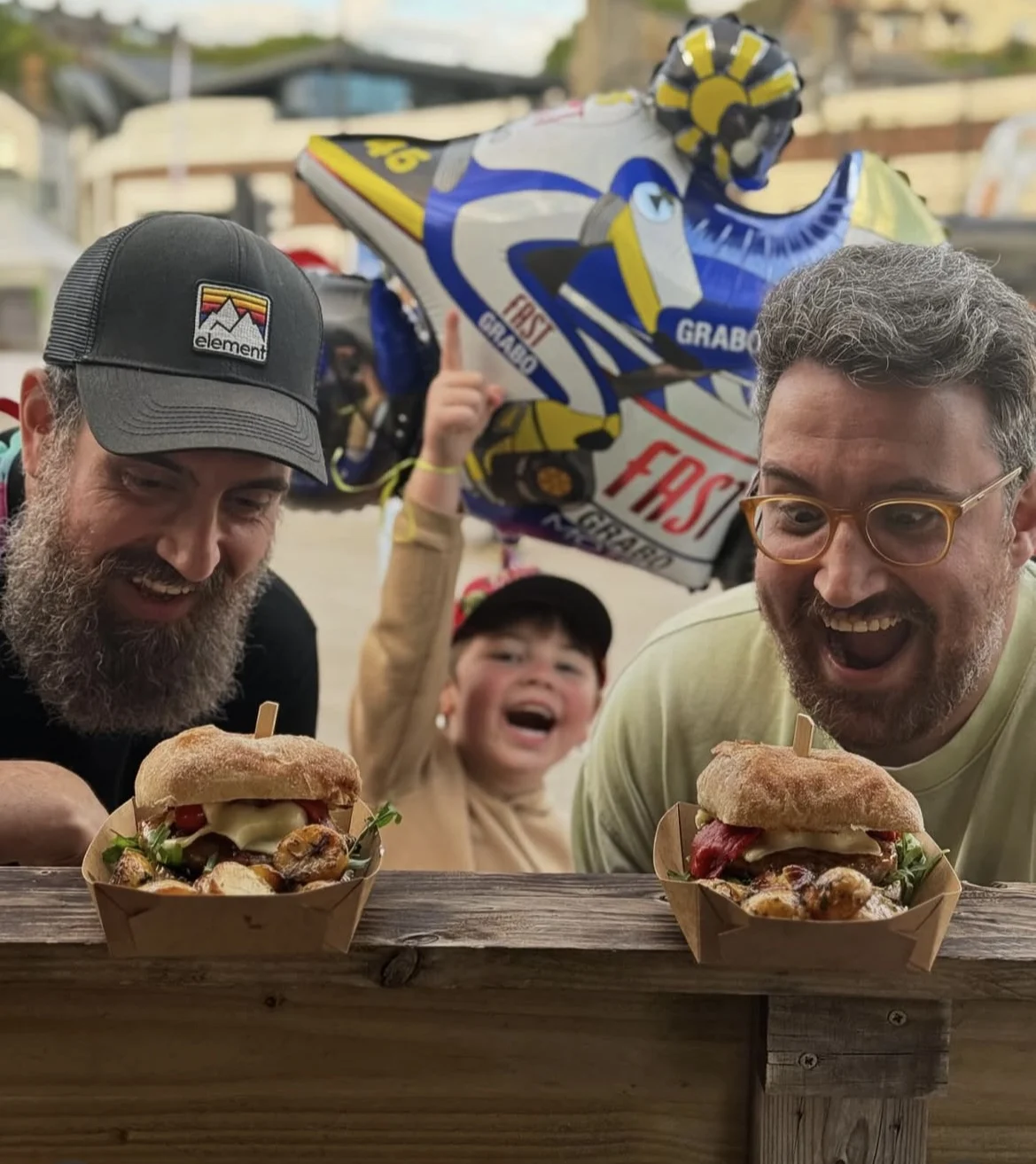 Two men and a smiling child with burgers from a street food stall at an event