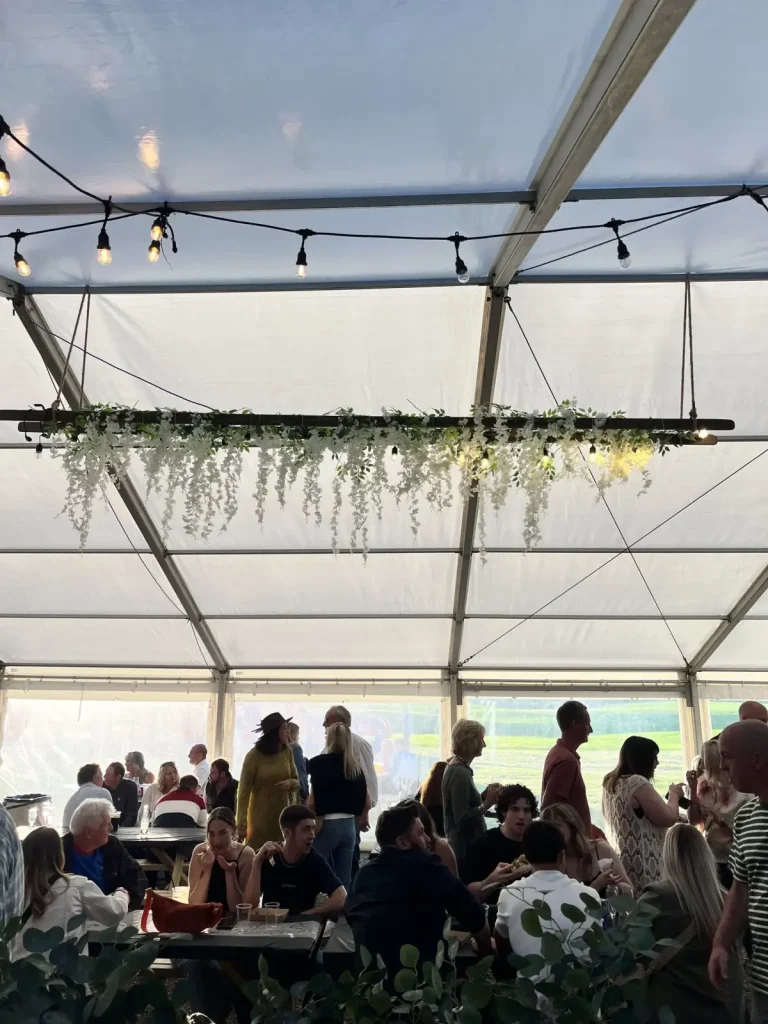 Crowds gathered in a marquee with hanging flowers and warm event lighting.