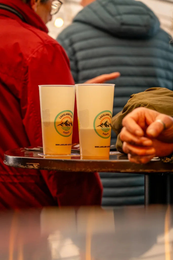 Two Lakeland Events cups on a table with people standing nearby.