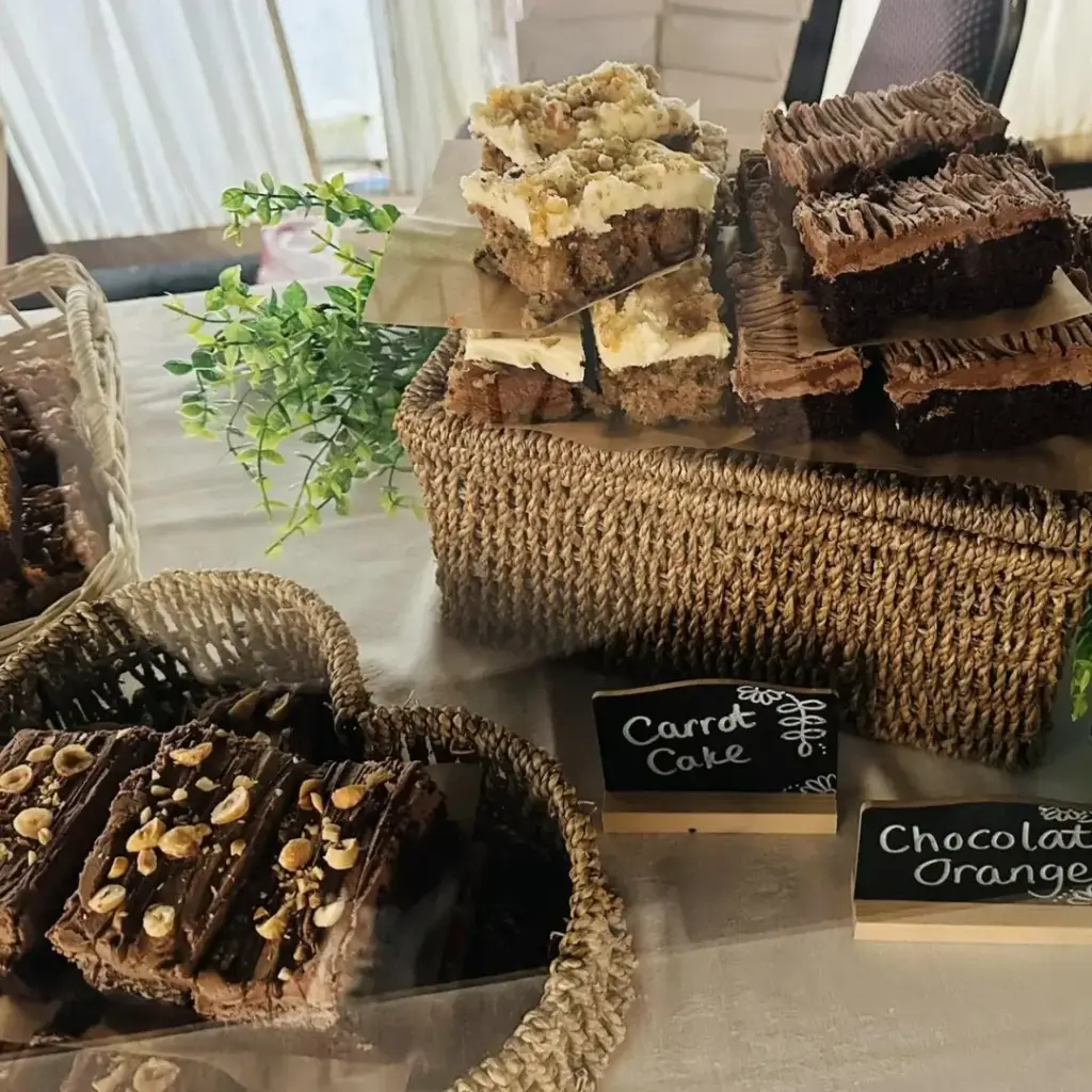 Display of assorted cake slices including carrot cake and chocolate varieties arranged in baskets and on a woven stand